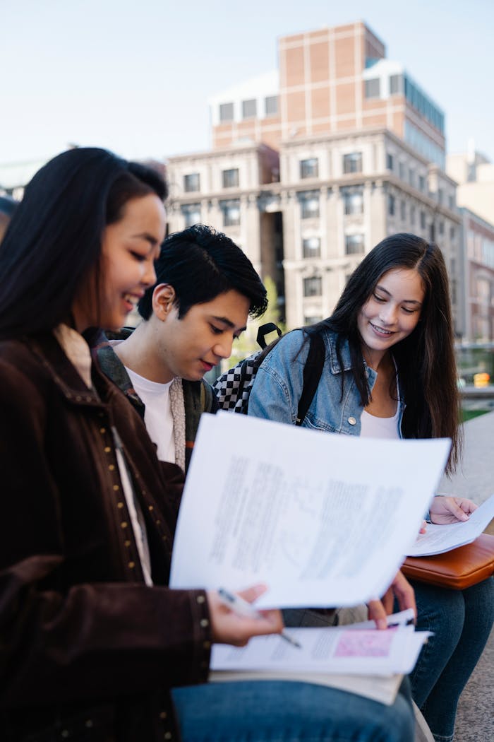 Group of young students reviewing documents outside a university building.